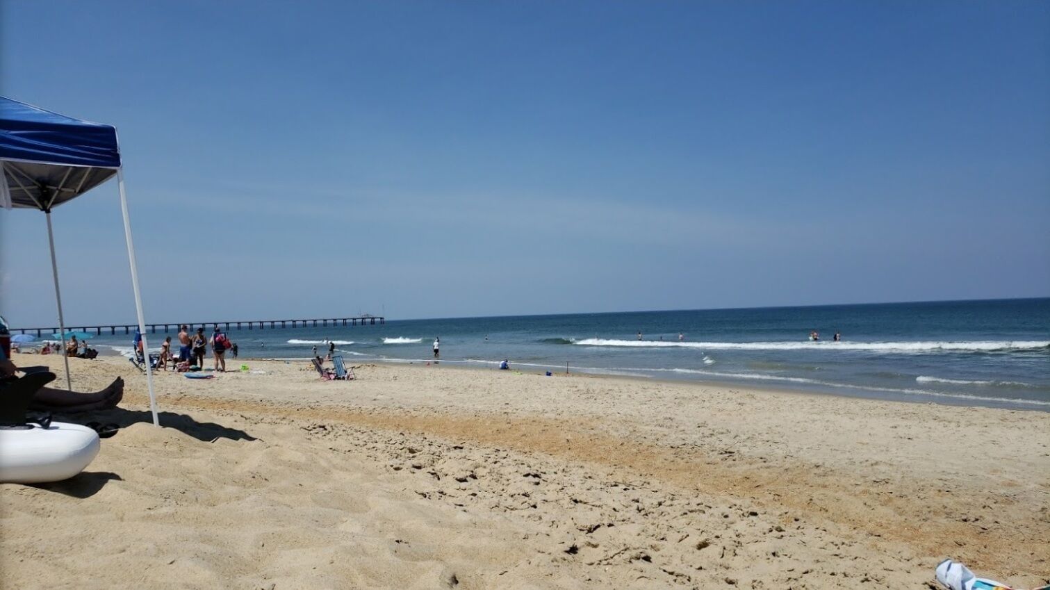 Une plage avec une jetée en arrière-plan, un ciel dégagé et des gens qui profitent de l’eau.