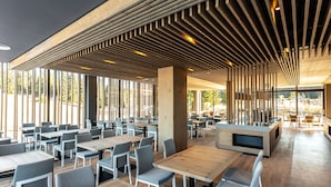 A modern restaurant with wooden tables and chairs, large windows, and a slatted ceiling design. - Hotel Monti Spa&Wellness (Hadzici)