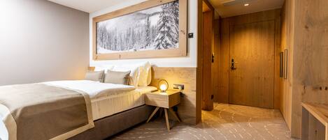 A modern hotel room with a large bed, a bedside table with a lamp, a framed picture on the wall, and a wooden wardrobe.