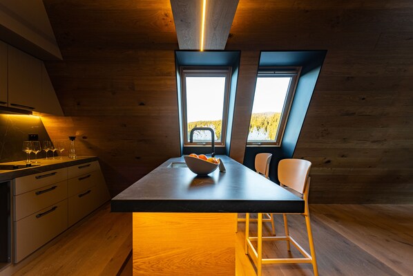 A modern kitchen with a central island, wooden walls, and large windows offering a view of the outdoors.