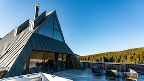 A modern, triangular-shaped building with a glass entrance and a hot tub on the patio. - Hotel Monti Spa&Wellness (Hadzici)