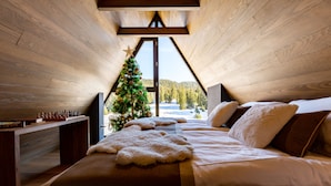 A cozy bedroom with a wooden ceiling, a Christmas tree, a bed with pillows, and a chessboard on a nightstand. - Hotel Monti Spa&Wellness (Hadzici)