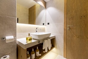 A modern bathroom with a large mirror, a white sink, and wooden cabinetry. - Hotel Monti Spa&Wellness (Hadzici)