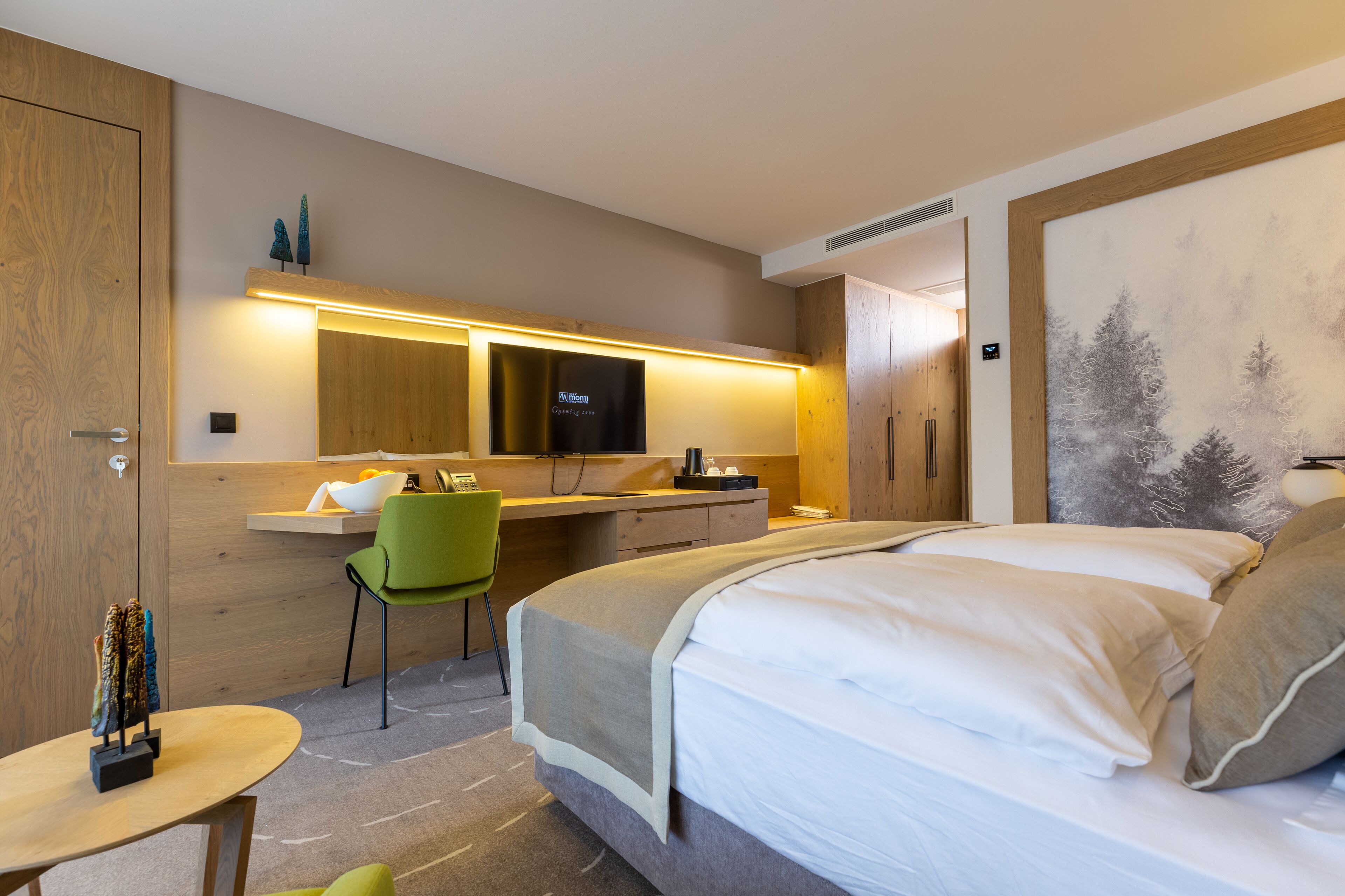 Een moderne hotelkamer met een bed, bureau, stoel en een schilderij aan de muur.