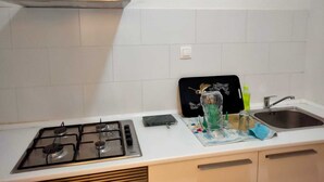 Ett kök med en gasspis, en rostfri köksfläkt, en svart skärbräda, en vas av glas och en diskho.