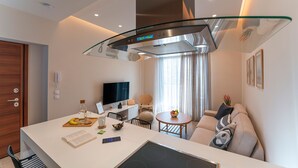Una cucina moderna con isola centrale, zona pranzo con tavolo rotondo e angolo living con divano e TV.