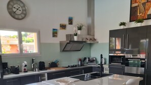Una cocina moderna con una isla central, taburetes de bar, electrodomésticos de acero inoxidable y un reloj en la pared.
