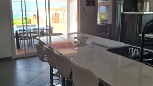 Una cocina moderna con una isla grande, un comedor con sillas y vistas al exterior.