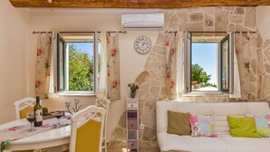 A cozy room with a stone wall, a white sofa, a dining table with chairs, and a clock on the wall. - Dubrovnik Chalets - 2 Charming Stone Houses (Konavle)