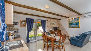 A spacious living area with a dining table, chairs, a sofa, and a kitchen with a sink and cabinets. - Dubrovnik Chalets - 2 Charming Stone Houses (Konavle)