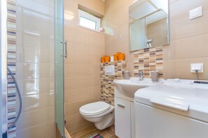 A modern bathroom with a glass shower enclosure, a toilet, a sink with a mirror, and a tiled backsplash.