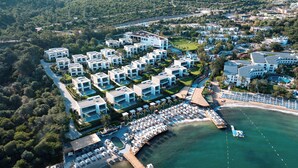 Eine Luftaufnahme eines Küstenresorts mit modernen Villen, einem Jachthafen und einem Strand mit Liegestühlen.