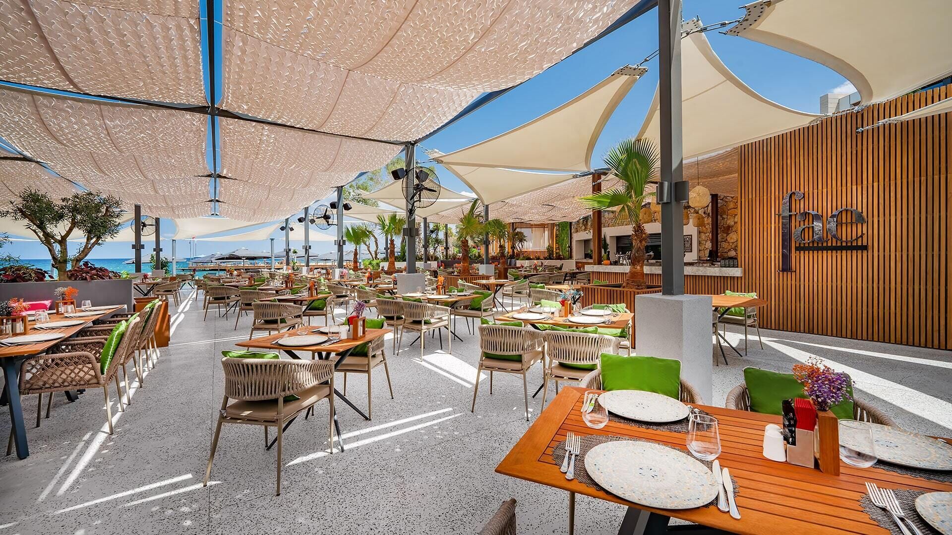 An outdoor dining area with tables and chairs, umbrellas, and a view of the ocean.