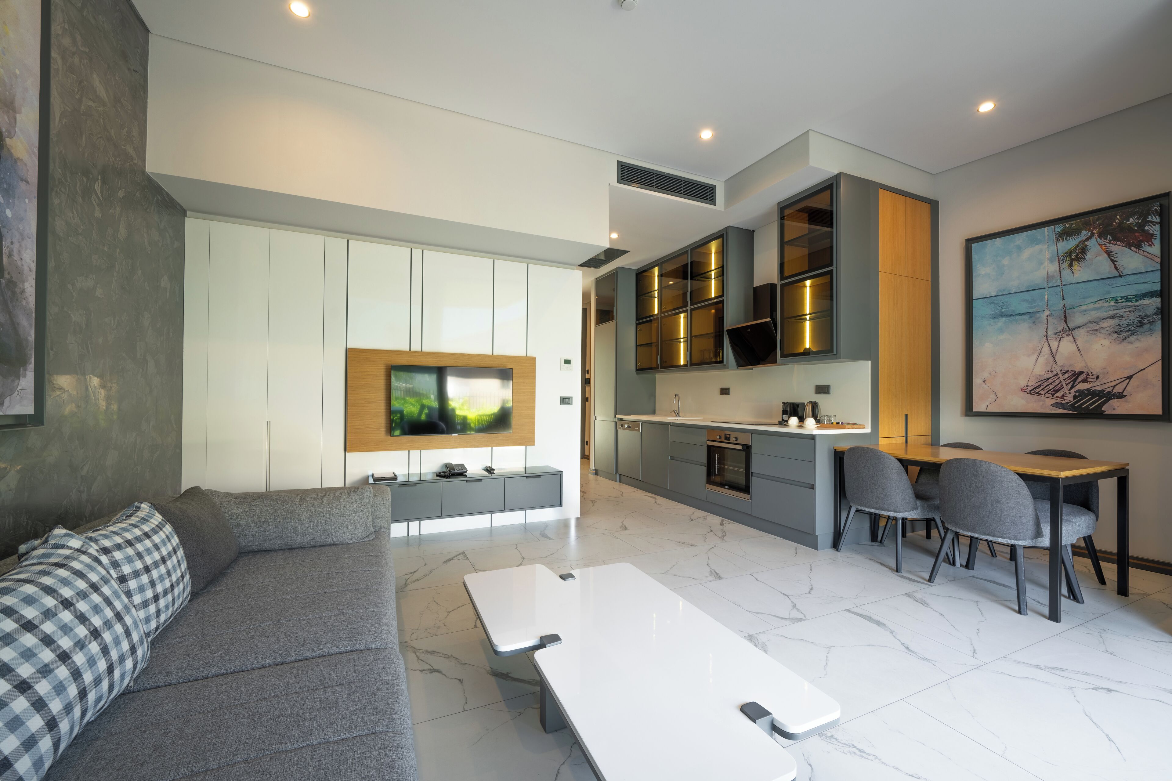 A modern living room with a grey sofa, a flat-screen TV, and a dining area with a table and chairs.