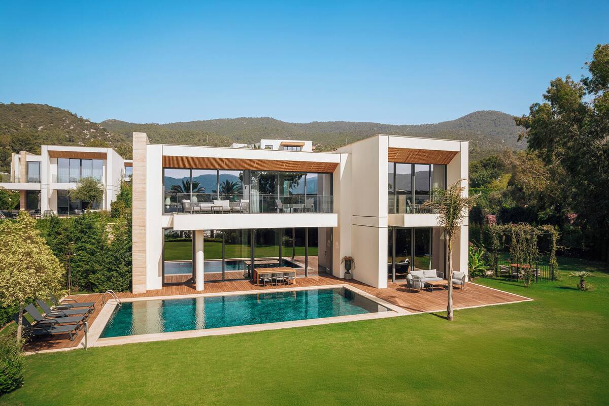 Uma casa moderna de dois andares com piscina, mobiliário para áreas externas e vista para a paisagem ao redor.