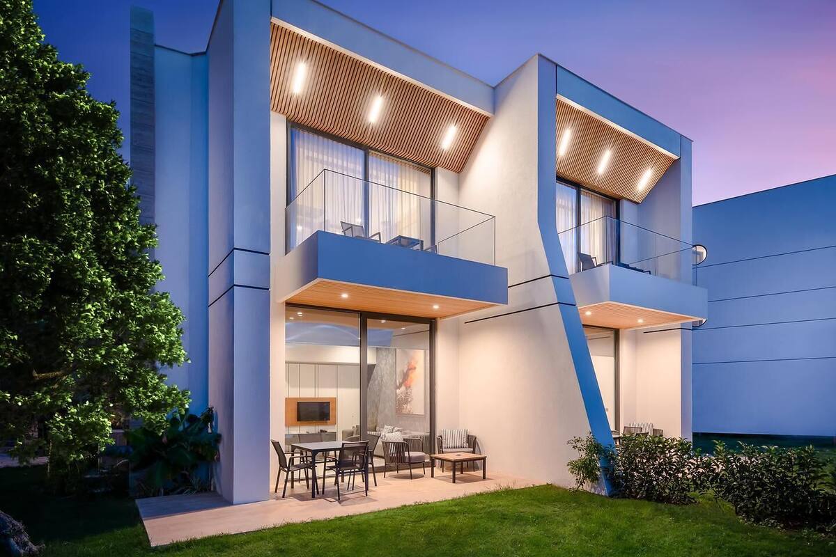 Uma casa moderna de dois andares com telhado plano, janelas grandes e varanda.