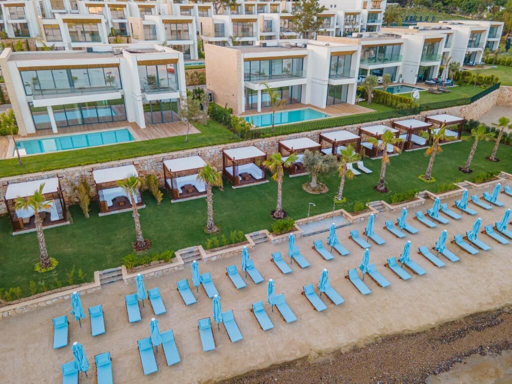 Un moderno complejo turístico con varias construcciones, piscina y zona de playa con tumbonas.