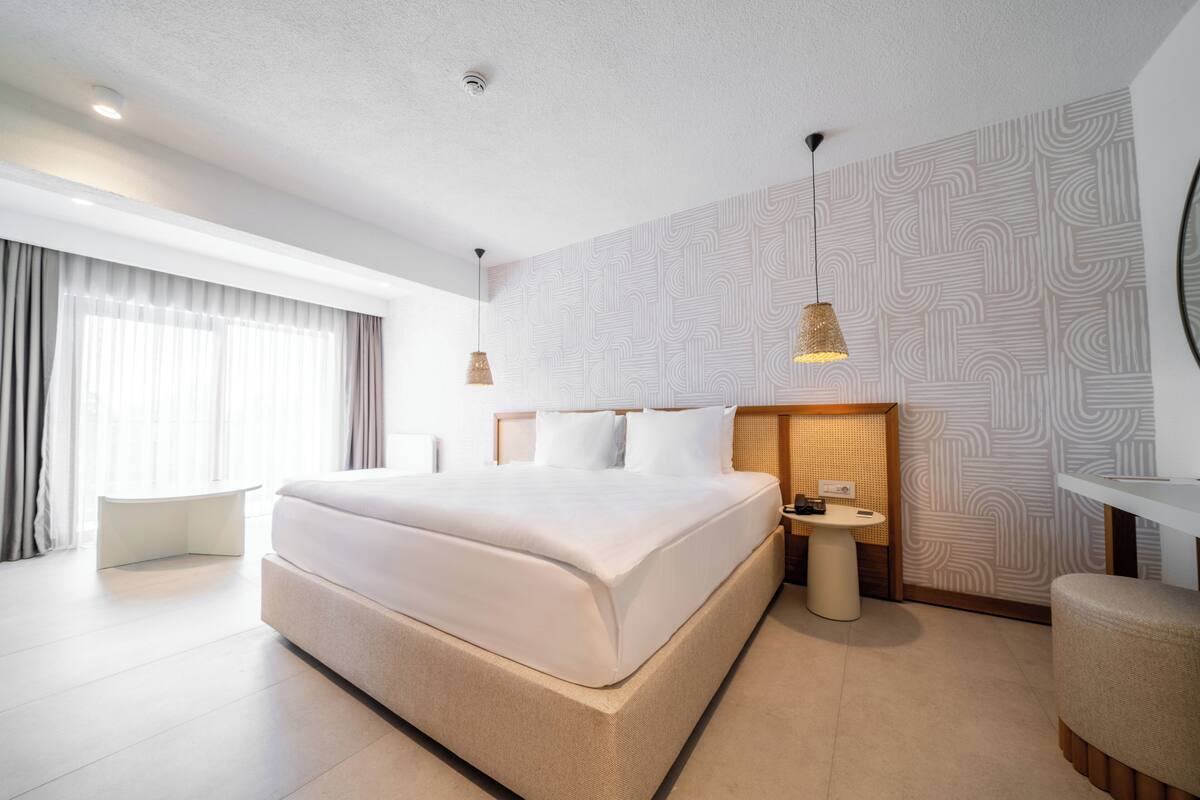 Quarto de hotel moderno com uma cama grande, mesa de cabeceira e uma pequena mesa redonda.
