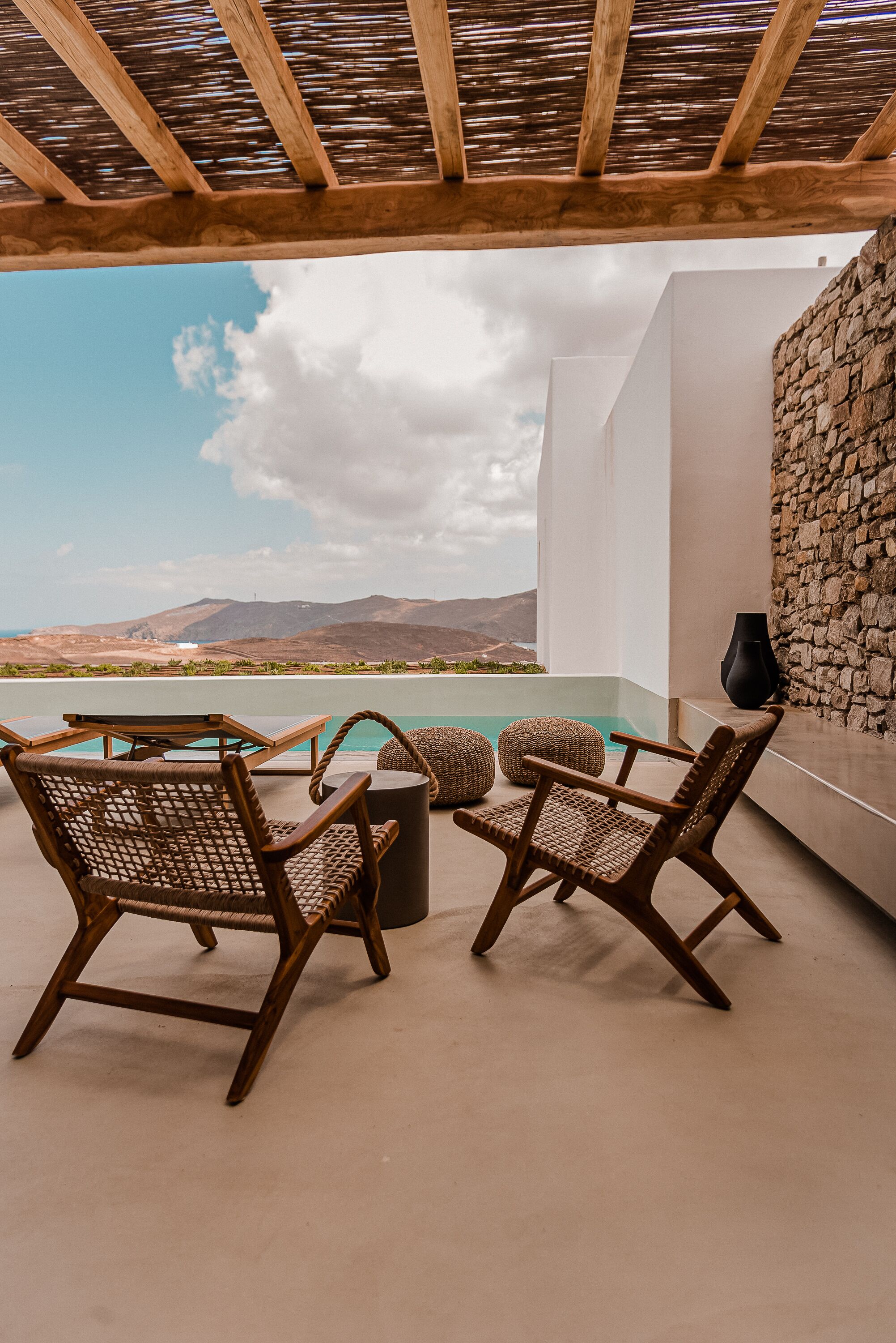 Eine Terrasse mit Korbstühlen und einem Tisch, mit Blick auf einen Pool und Berge.