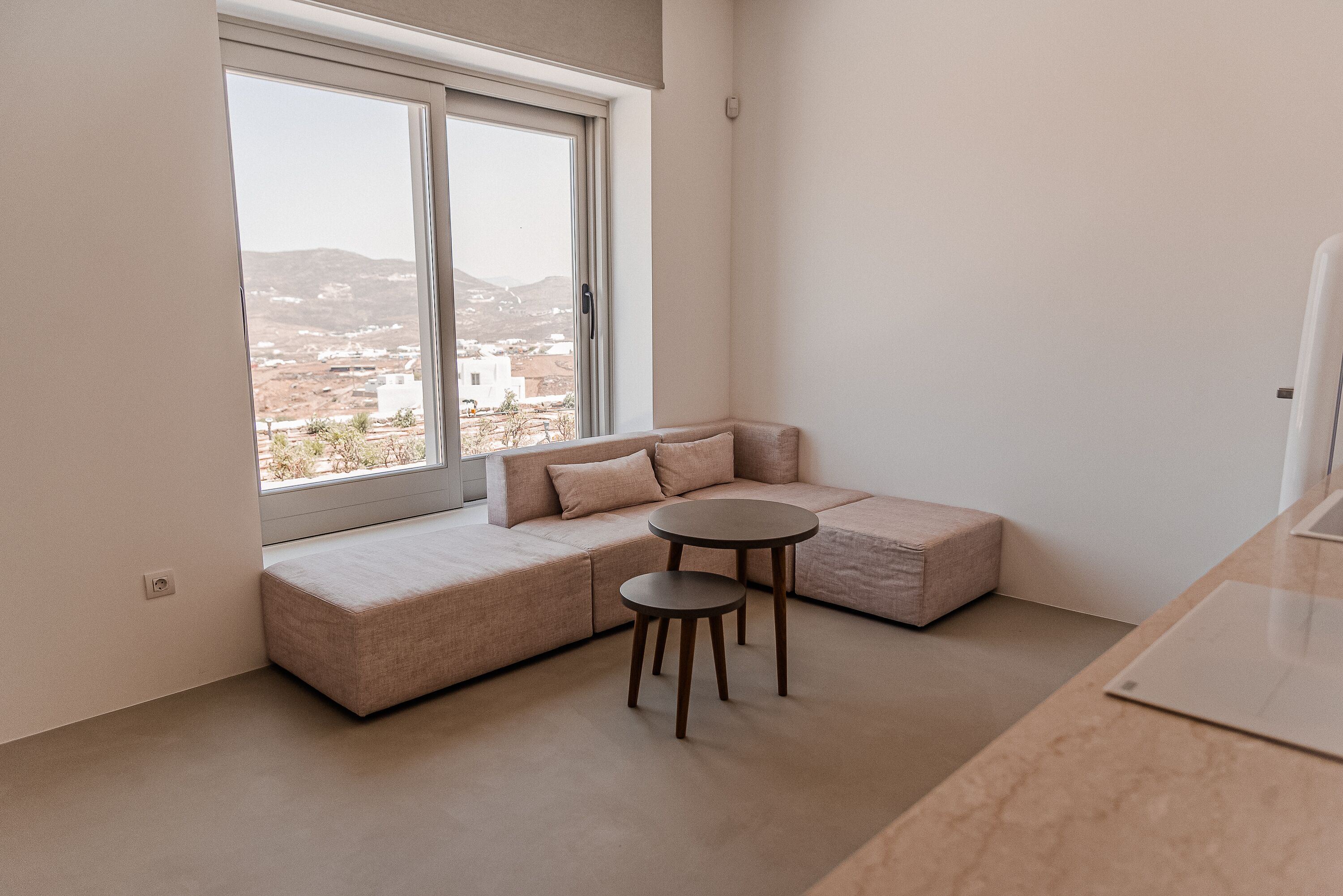Ein modernes Wohnzimmer mit großem Fenster, einer Couch, einem kleinen runden Tisch und einer Küchenzeile.
