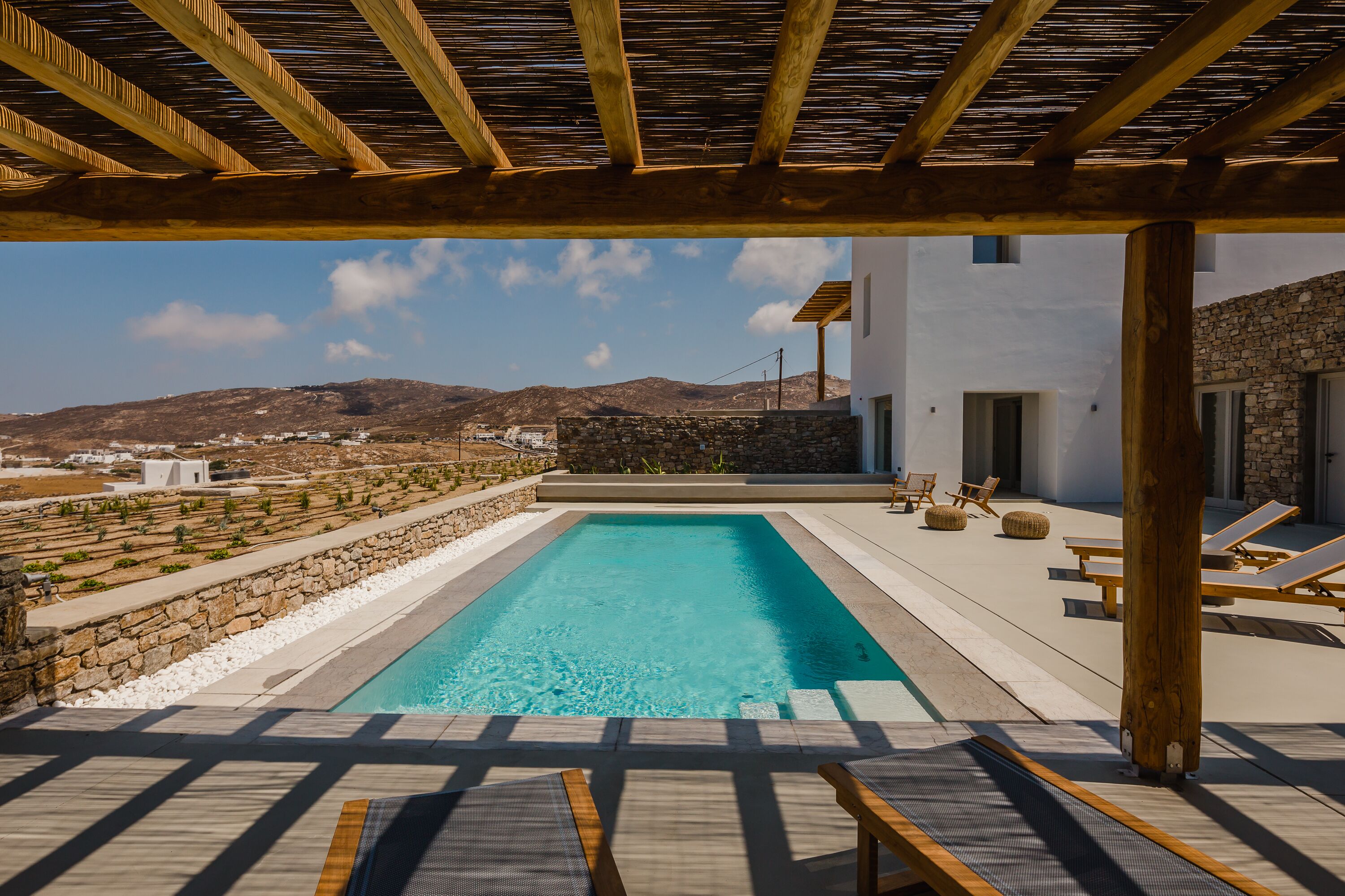 Un espace piscine avec vue sur les montagnes, une pergola en bois et des chaises longues.