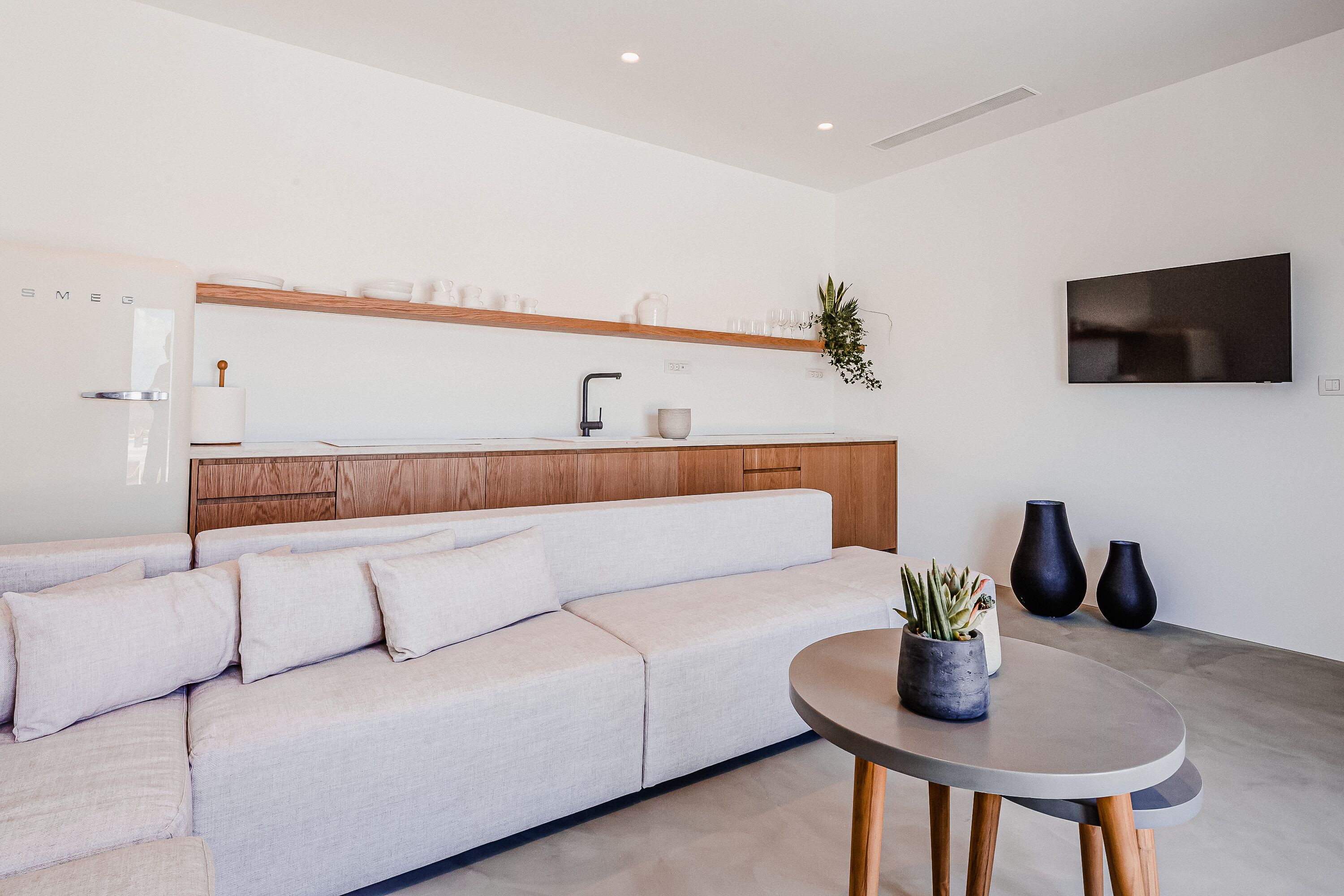 Ein modernes Wohnzimmer mit einer Couch, einem Couchtisch und einer Küchenzeile mit einer Holz Arbeitsplatte sowie einem an der Wand befestigten Fernseher.