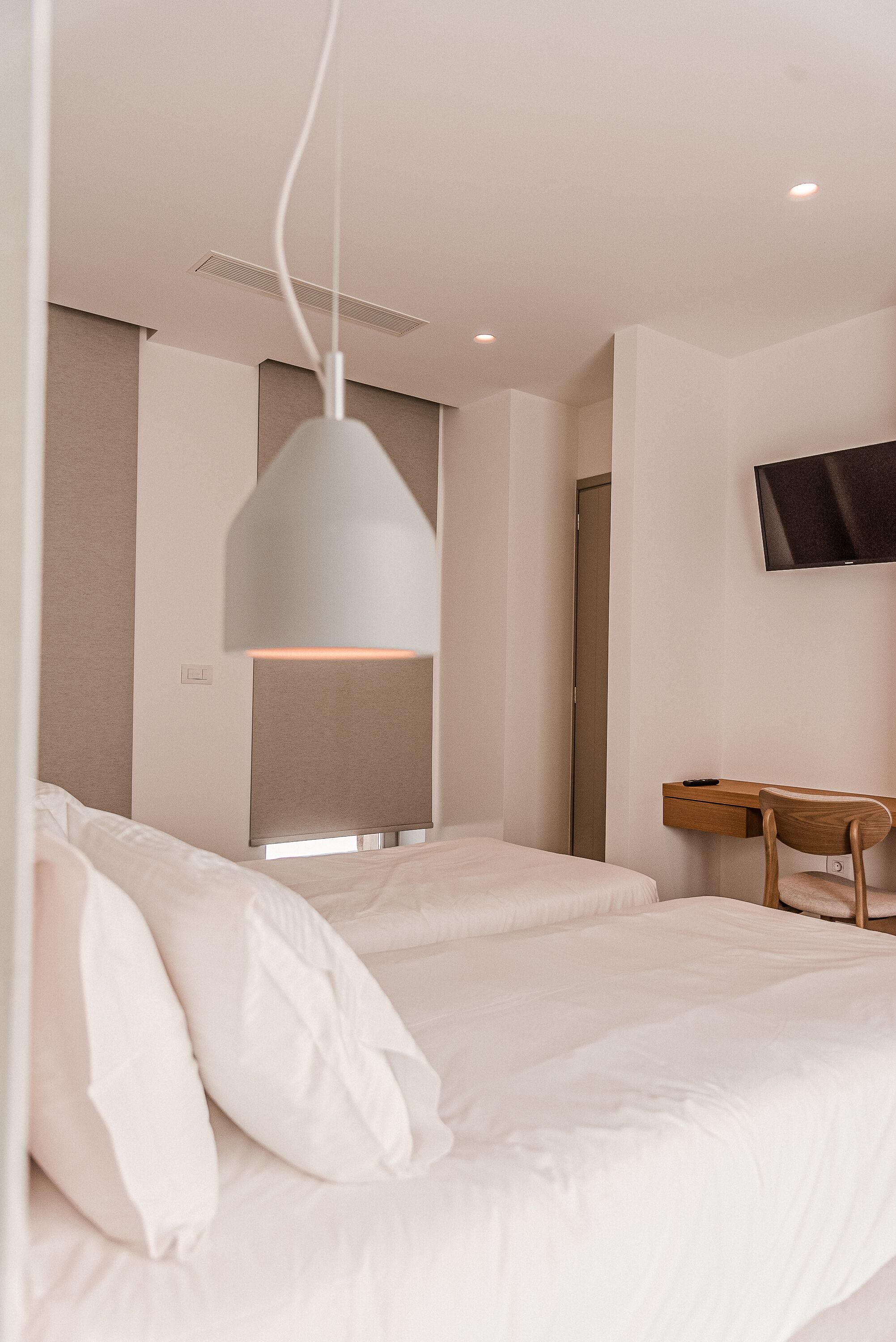 A modern hotel room with a bed, a desk, and a TV mounted on the wall.