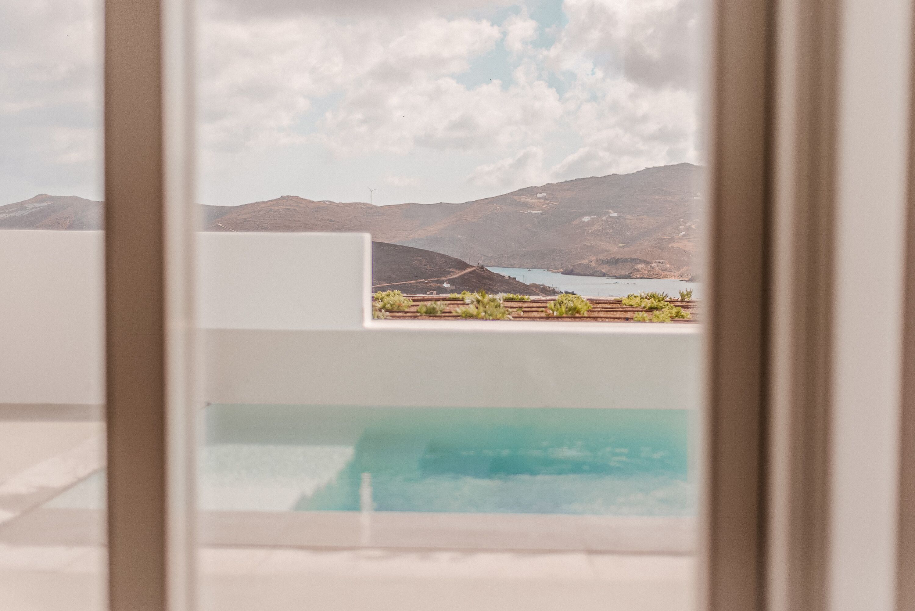 Vista desde una ventana a un área de piscina, con paisaje montañoso al fondo.