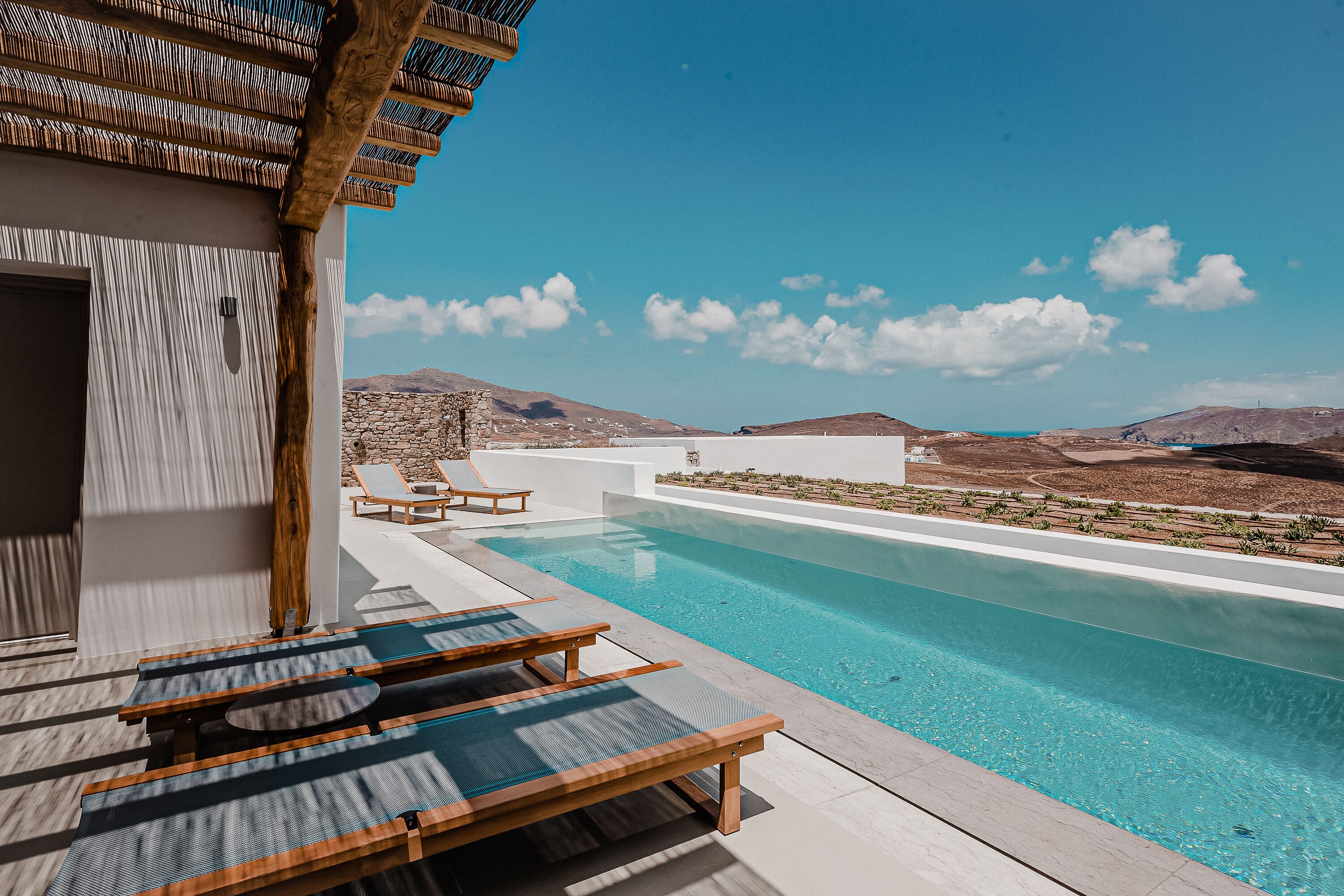 A pool area with lounge chairs, a pergola, and a view of the landscape.