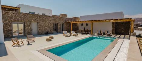 A modern outdoor pool area with stone walls, lounge chairs, and a pergola.