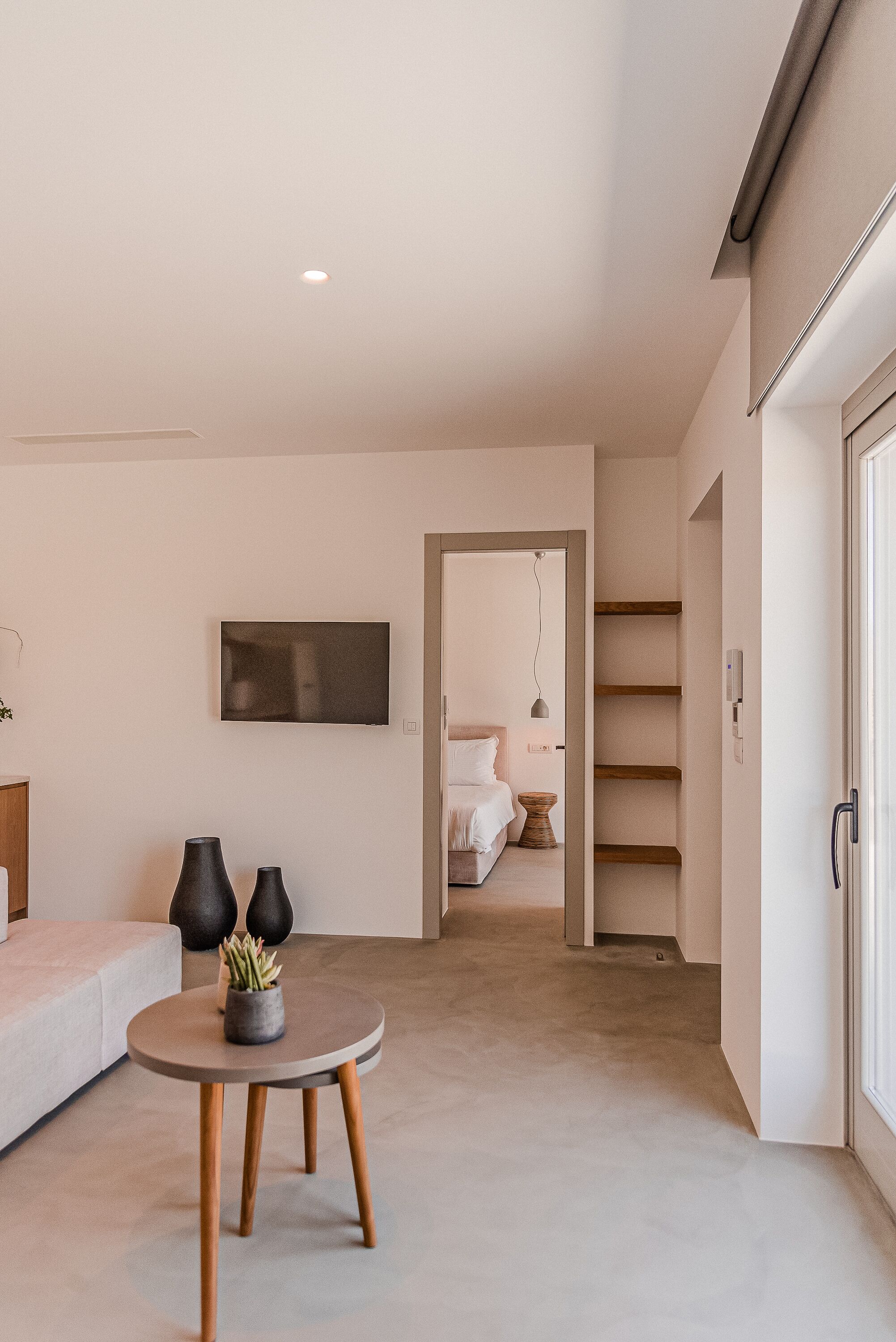 Una sala moderna con una mesa redonda, un sofá y un televisor montado en la pared. Una escalera conduce a otra habitación.