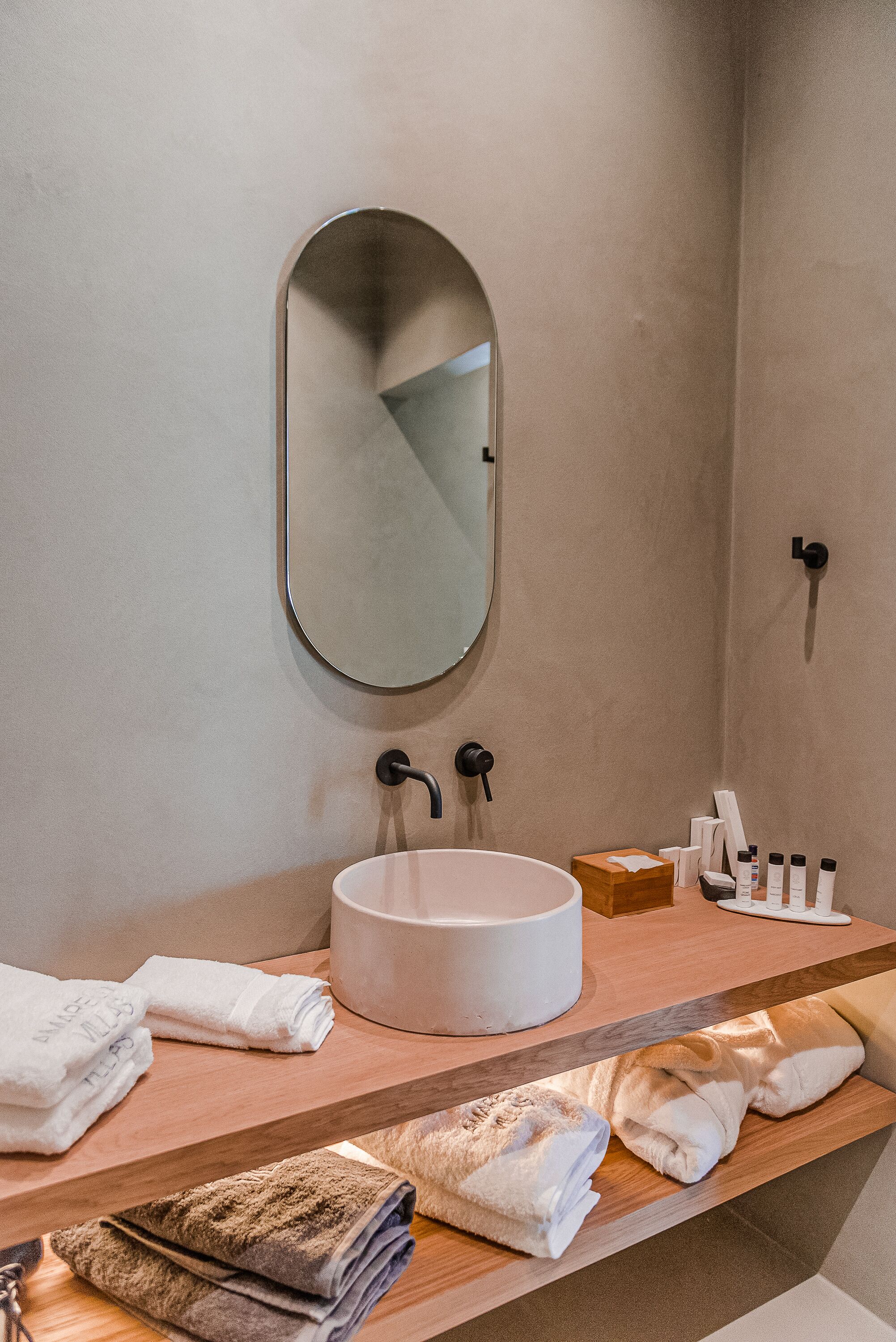A bathroom with a round mirror, a sink, and neatly folded towels on a wooden shelf.
