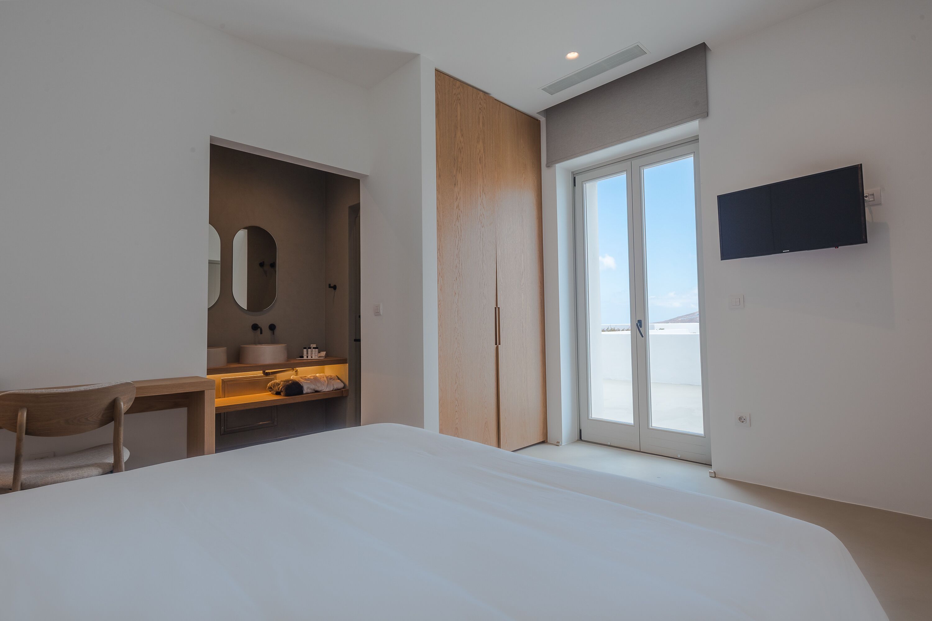 Una habitación de hotel moderna con una cama grande, un escritorio de madera, un baño con espejo y un televisor montado en la pared.