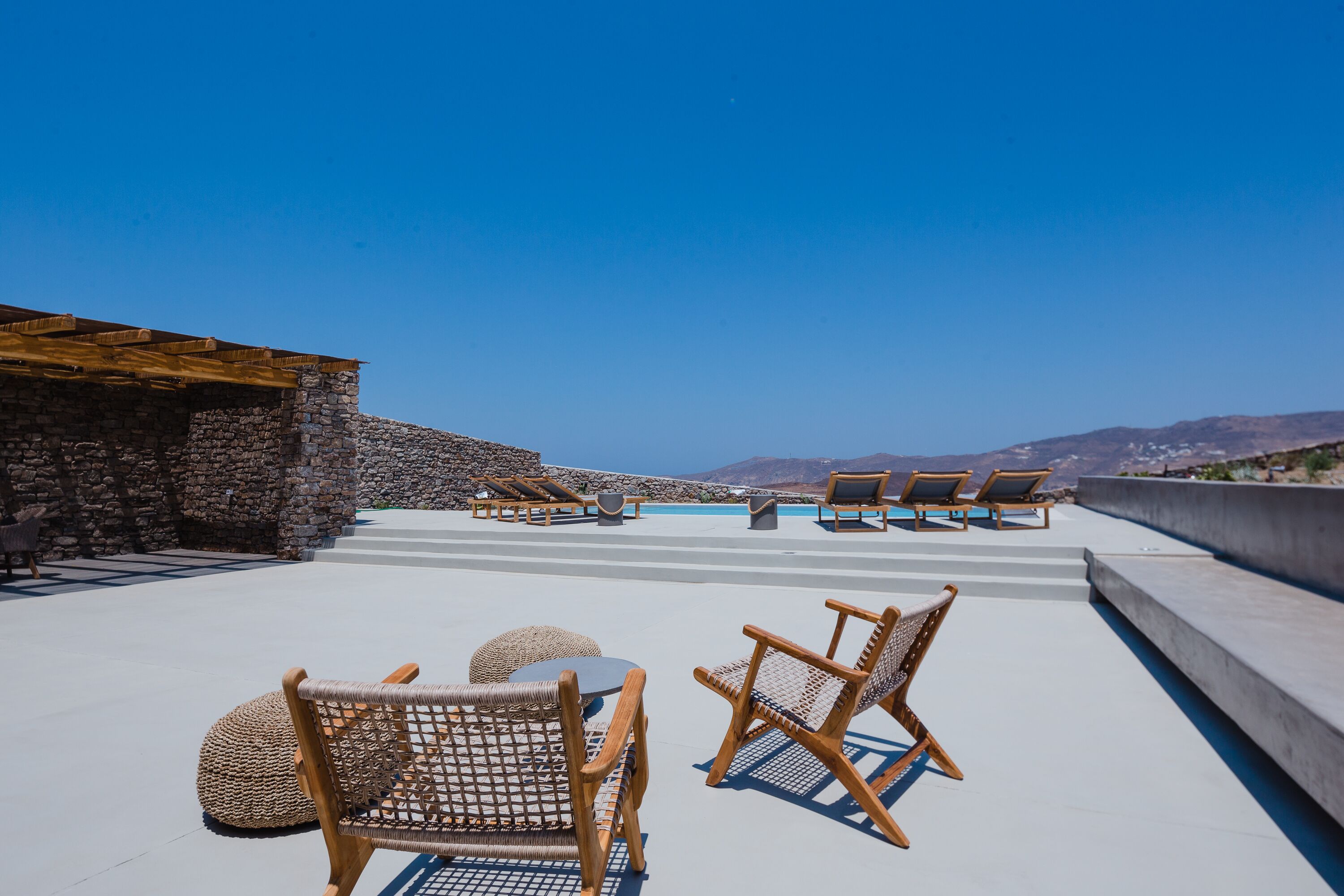 Una terraza en la azotea con paredes de piedra, sillones de descanso y una piscina.