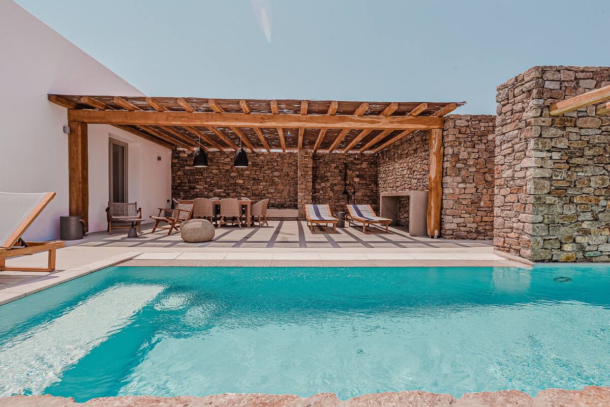 Ein Poolbereich mit Pergola, Steinmauern und Liegestühlen.