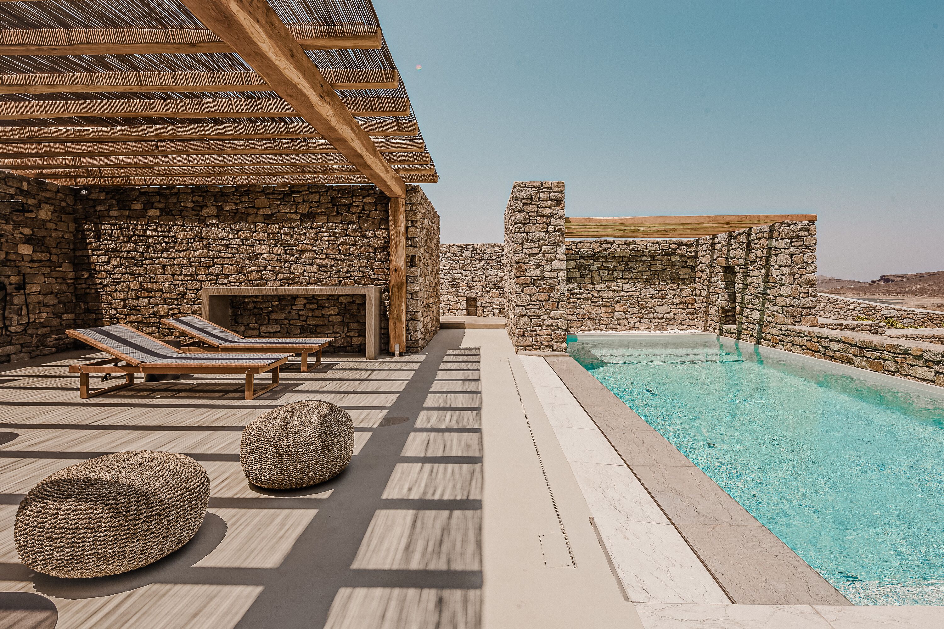 A poolside area with stone walls, lounge chairs, and a clear blue pool.