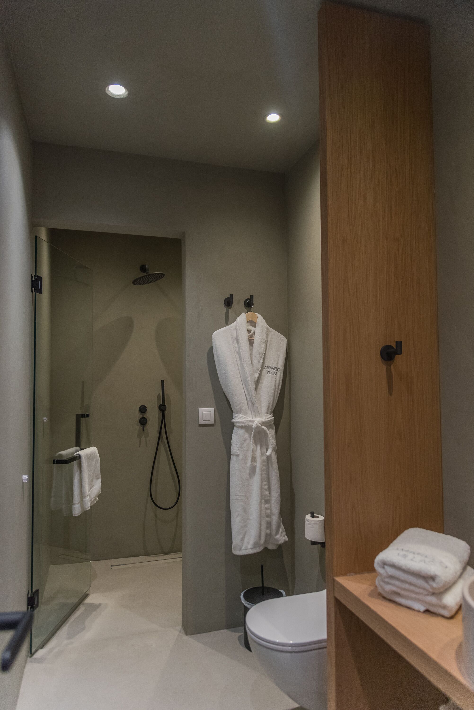 Une salle de bain moderne avec une douche à parois de verre, un meuble-lavabo en bois et un peignoir blanc accroché au mur.