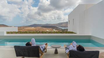 Two lounge chairs facing a pool with a view of hills and a body of water.