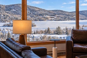 A room with a view of a snowy landscape, a sofa, a lamp, and a table. - Tremblant Prestige - Altitude 168-9 (Mont-Tremblant)