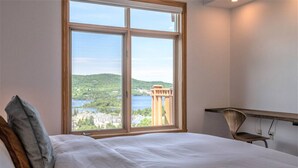 Habitación de hotel con un ventanal grande que ofrece vistas a un lago y edificios.