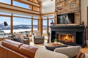 Una sala de estar acogedora con chimenea, sofá de cuero y un amplio ventanal con vistas panorámicas.