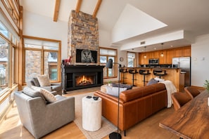 A modern living room with a fireplace, leather sofas, and a kitchen with wooden cabinets. - Tremblant Prestige - Altitude 168-9 (Mont-Tremblant)