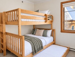 A bunk bed with a wooden frame, white bedding, and a window with a view of a building.