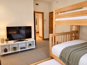 A bedroom with a bunk bed, a television on a white stand, and a small shelf with plants. - Tremblant Prestige - Altitude 168-9 (Mont-Tremblant)