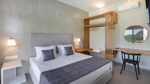 Ett modernt hotellrum med en stor säng, ett skrivbord och en stol. Det finns en garderob med en spegel, en luftkonditioneringsanläggning och utsikt över ett berg.