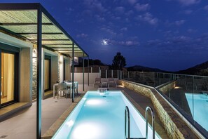 Piscina exterior con barandilla de cristal, sillas de descanso y pared de piedra.
