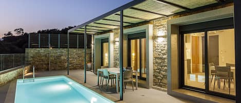 A modern outdoor pool area with a glass-enclosed patio, stone walls, and a dining setup.