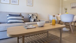 A modern living room with a sofa, a coffee table, a dining area with chairs, and a hanging light fixture.