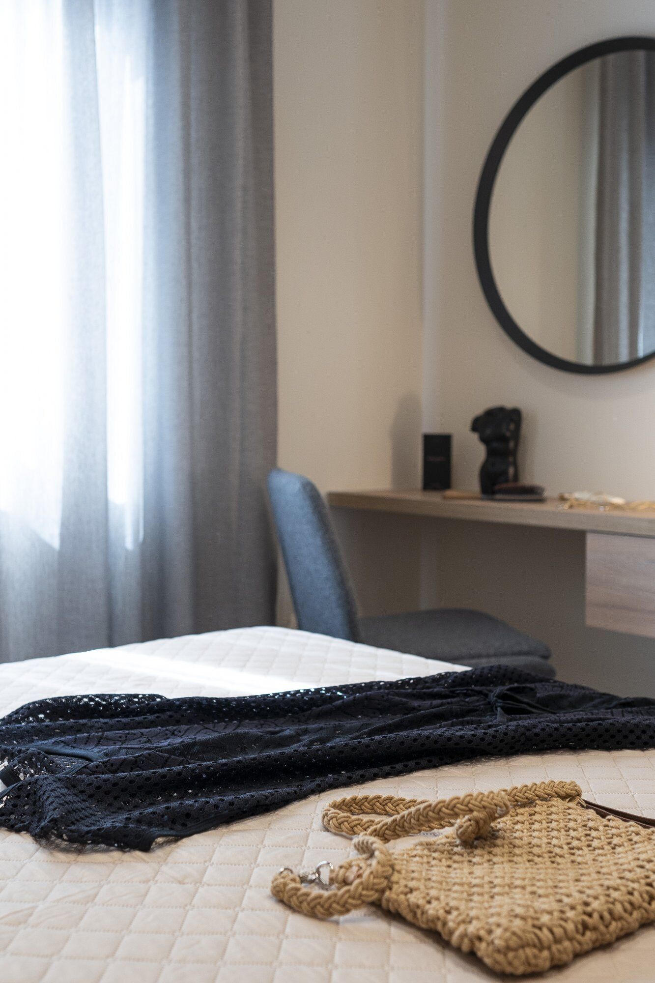 Ein Bett mit einer gesteppten Decke, einem schwarzen Spitzenaccessoire und einer braunen gewebten Tasche darauf.