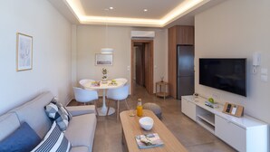 A modern living room with a sofa, a dining table with chairs, a coffee table, a TV, and a kitchen area with a refrigerator.